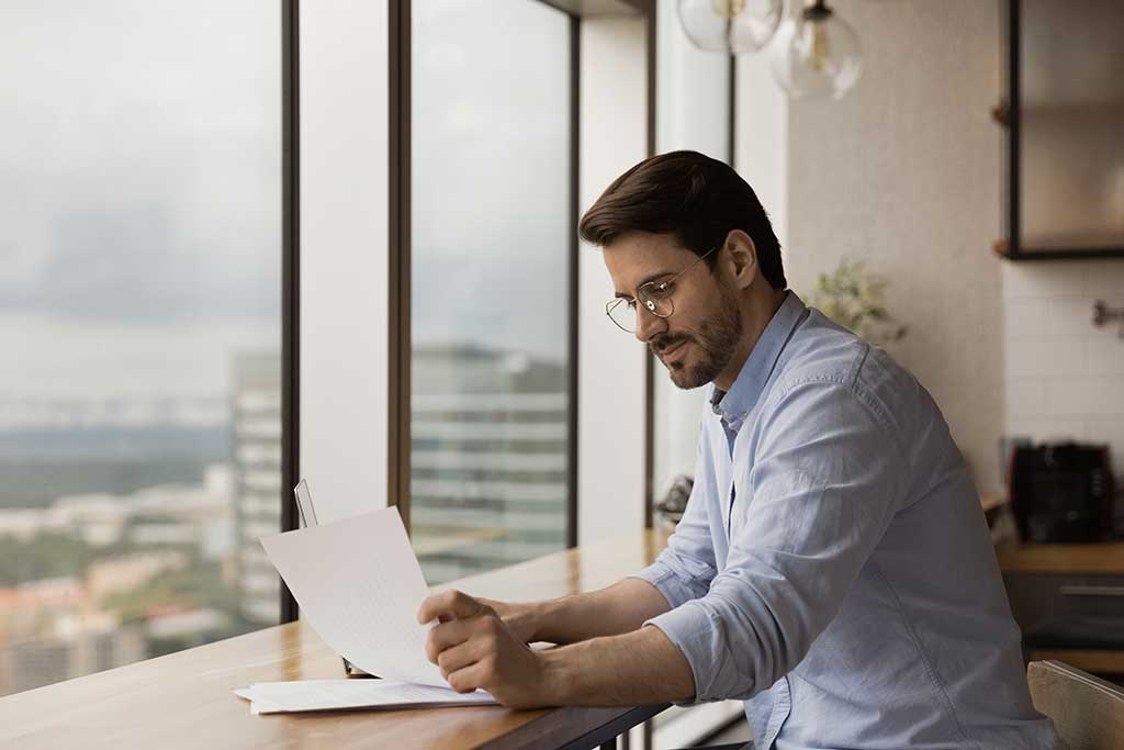 Successful businessman read paper document at work desk in studio apartment near panoramic window.